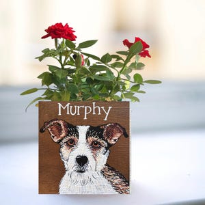 A potted plant with red roses and a wooden card featuring a dog's face.