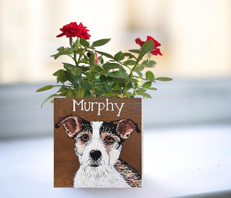 A potted plant with red roses and a wooden card featuring a dog's face.