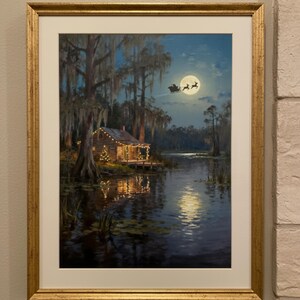 K&ouml;nnte beinhalten: Gerahmtes Gem&auml;lde einer n&auml;chtlichen Weihnachtsszene. Eine H&uuml;tte mit funkelnden Lichtern liegt an einem See, mit Vollmond und dem Schlitten des Weihnachtsmanns am Himmel. Das Kunstwerk ist in einem goldfarbenen Rahmen gerahmt.