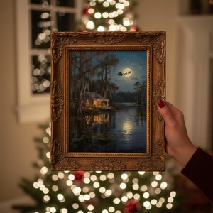 K&ouml;nnte beinhalten: Ein gerahmtes Gem&auml;lde, das eine n&auml;chtliche Sumpflandschaft mit einer H&uuml;tte zeigt, die von warmen Lichtern beleuchtet wird. Das Gem&auml;lde wird vor einem Weihnachtsbaum mit funkelnden Lichtern gehalten. Der Rahmen ist verziert und goldfarben, was das festliche Thema unterstreicht.