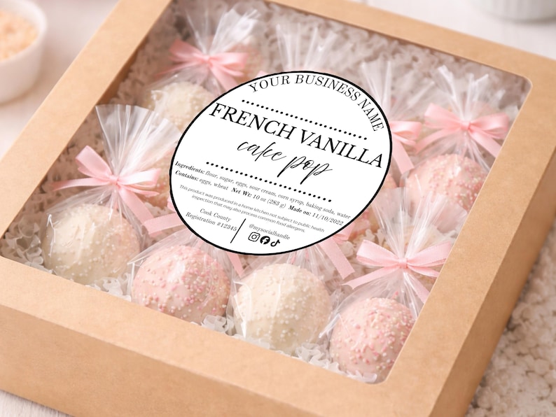 May include: A square cardboard box with a clear window containing individually wrapped cake pops. Each pop is tied with a light pink ribbon. A circular label reads: YOUR BUSINESS NAME, FRENCH VANILLA cake pop, Net Wt: 10 oz (283 g).