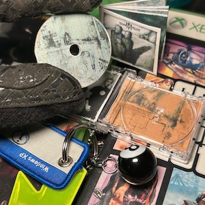 Könnte beinhalten: Eine Sammlung von CDs, ein Schlüsselanhänger und ein schwarzer 8-Ball-Anhänger. Die CDs haben abstrakte Kunst. Der Schlüsselanhänger hat ein blau-weißes Etikett mit dem Text "Windows XP". Der 8-Ball-Anhänger ist an einem Schlüsselanhänger befestigt.