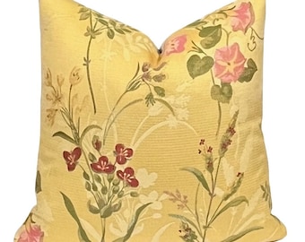 Op de afbeelding: Een vierkant sierkussen met een gele achtergrond en een bloemenpatroon. Het patroon bevat roze, rode en groene bloemen en bladeren. Het kussen heeft een zachte, getextureerde uitstraling en is waarschijnlijk gemaakt van stof.