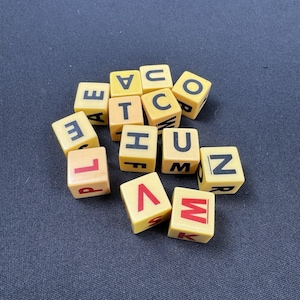 May include: A collection of yellow letter tiles with black and red letters. The tiles are scattered on a dark blue surface. The letters on the tiles include A, C, E, F, H, L, M, N, O, P, R, T, U, V, and W.