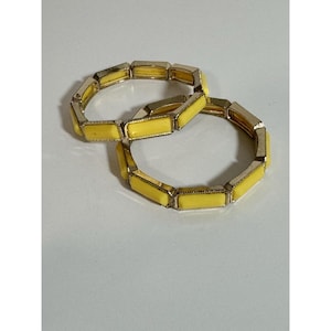 May include: Two yellow and gold-toned bracelets. Each bracelet is made of rectangular yellow segments connected by gold-colored metal. The bracelets are displayed on a white surface.
