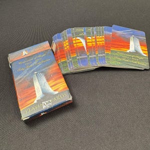 May include: A deck of playing cards with a box featuring the text "Centennial of Flight 1903-2003 Kitty Hawk, North Carolina." The cards and box have a sunset background with a monument. The cards are fanned out.