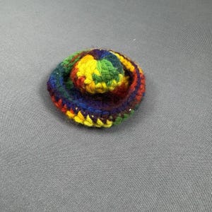 May include: A small, round, crocheted item in a spiral pattern. The item features a vibrant array of colors, including yellow, green, red, and blue. The item is likely handmade and could be a decorative element or a small accessory.