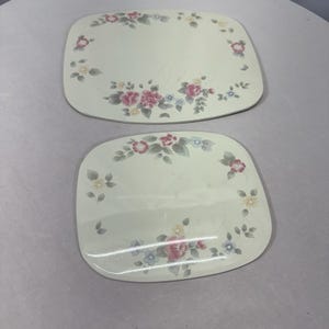May include: Two off-white, rectangular plates with rounded corners. Each plate features a floral design with pink, blue, and yellow flowers, along with green leaves. The floral pattern is arranged around the edges of the plates.
