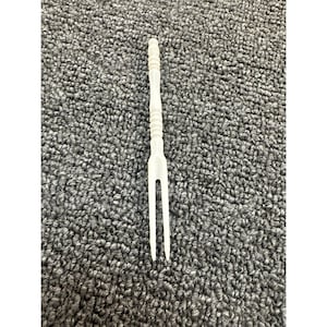 May include: A white, two-pronged appetizer fork with a long, slender handle featuring a series of horizontal ridges and a smooth, rounded top. The utensil is crafted from a solid, opaque material with a matte finish and a simple, functional design.