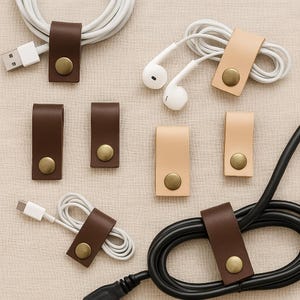 Puede incluir: Surtido de organizadores de cables de cuero en marr&oacute;n y tostado con detalles en lat&oacute;n. Los organizadores est&aacute;n dise&ntilde;ados para sujetar y ordenar cables, cables y alambres.