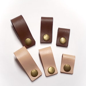 May include: Six leather drawer pulls with brass accents. The pulls are in two colors: brown and light pink.