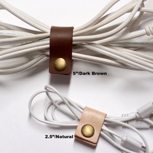 Puede incluir: Dos organizadores de cables de cuero, uno marr&oacute;n oscuro y otro natural, con detalles en lat&oacute;n. El organizador marr&oacute;n oscuro mide 5 pulgadas de largo y el organizador natural mide 2,5 pulgadas de largo.