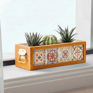 May include: A rectangular wooden planter box with colorful ceramic tile accents. The box contains three small succulents and a cactus. A metal clasp is on the side of the planter.