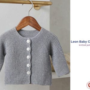 Puede incluir: Un cárdigan gris de punto para bebé, con cuello redondo y mangas largas, abrochado con botones blancos. La chaqueta está colgada de una percha de madera. El texto "Leon Baby Cardigan knitted jacket" es visible.