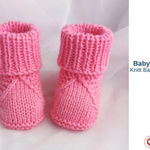 May include: A pair of pink knitted baby booties. The booties have a ribbed cuff and a textured design on the front. The text "Baby Steps Knitt Baby Shoes" is visible in the image.