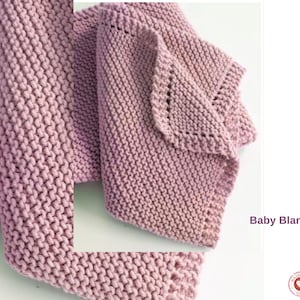 May include: A knitted baby blanket in a dusky pink hue. The blanket has a textured stitch and a decorative edge. The words "Baby Blanket" are printed in a purple font on the right side of the image.