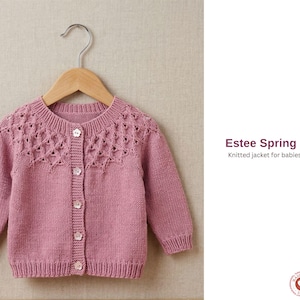 Puede incluir: Una chaqueta de bebé de punto rosa polvoriento con canesú decorativo y cierre de botones, colgada de una percha de madera. La chaqueta tiene mangas largas y puños acanalados. El texto dice "Estee Spring Jacket" y "Knitted jacket for babies and children."