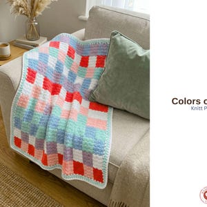 May include: A colorful, handmade knit blanket with a checkerboard pattern in shades of red, pink, blue, and white. The blanket is draped over a beige sofa with a green pillow. The text "Colors of Love Knitt Pattern" is visible.