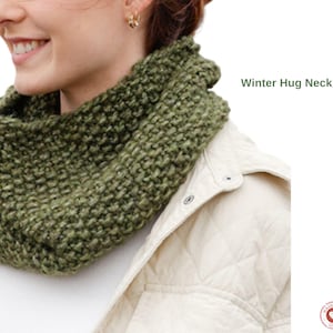 May include: A green knit neck warmer, with the text "Winter Hug Neck warmer" in green. The neck warmer is made of a chunky knit material and is wrapped around the neck. The person is wearing a cream-colored jacket.