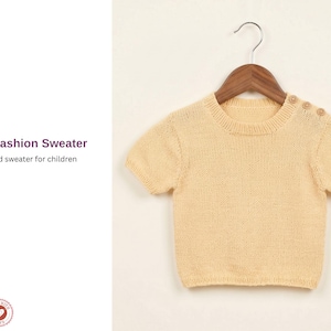 May include: A light yellow knitted sweater for children, with short sleeves and a crew neck, hangs on a wooden hanger. The sweater has three small buttons on the shoulder. The text "Paris Fashion Sweater" and "Knitted sweater for children" is on the left.
