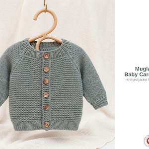 Könnte beinhalten: Ein grauer gestrickter Baby-Cardigan mit Holzknöpfen, präsentiert auf einem Holzbügel. Der Cardigan hat lange Ärmel und eine gerippte Textur. Der Text auf dem Bild lautet "Mugla Baby Cardigan Knitted jacket for baby."