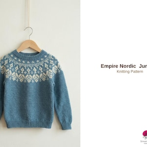 May include: A blue knitted jumper with a white patterned yoke, hanging on a wooden hanger. The jumper has long sleeves and a round neckline. The text "Empire Nordic Jumper Knitting Pattern" is visible on the right side.