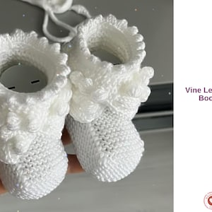Puede incluir: Un par de patucos de bebé blancos tejidos con un diseño de hoja de vid alrededor del tobillo. Los patucos están hechos a mano y presentan un borde texturizado y con volantes. El texto "Vine Leaf Baby Booties" es visible en la imagen.