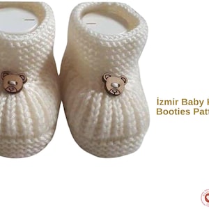 Pode incluir: Um par de botinhas de bebé de malha de cor creme. Cada botinha apresenta um pequeno botão de madeira em forma de urso. O texto "Izmir Baby Knit Booties Pattern" é visível à direita. Um artigo de bebé encantador.
