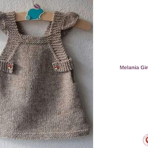 Pode incluir: Vestido de malha castanho claro, feito à mão, para menina, pendurado num cabide de madeira com uma decoração de coelho azul. O vestido tem botões em forma de cogumelo e o texto "Melania Girl Dress".