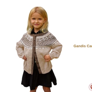 May include: A beige cardigan with a geometric pattern on the yoke and sleeves. The cardigan has a button-up front and is worn by a young person. The text "Gandis Cardigan" is displayed in brown.