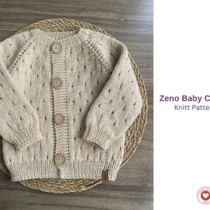 May include: A cream-coloured baby cardigan with a button-up front and round neckline. The knitted sweater features a textured design with small openings and is displayed on a woven mat. The text "Zeno Baby Cardigan Knitt Pattern Set" is visible.