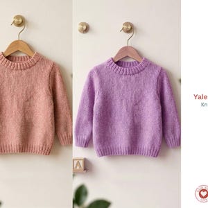 May include: Two children's sweaters, one in a soft pink and the other in a light purple, hang on wooden hangers. The sweaters have a crew neck and long sleeves. The text "Yales Pullover Knitt Pattern" is visible on the right side of the image.