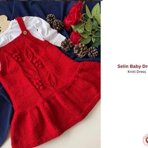 Może przedstawiać: Czerwona dzianinowa sukienka dla dziecka z białą koszulką z długim rękawem pod spodem. Sukienka ma teksturowany wzór z dekoracyjnymi pomponami i wzorami liści. Sukienka ma falbankę i drewniane guziki. Widoczny jest tekst "Selin Baby Dress Knitt Dress".