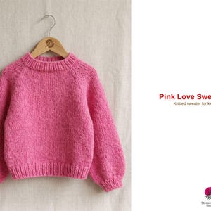 Könnte beinhalten: Ein leuchtend rosa Strickpullover für Kinder, der an einem Holzbügel hängt. Der Pullover hat einen runden Ausschnitt und lange Ärmel. Der Text "Pink Love Sweater" und "Knitted sweater for kids" ist rechts zu sehen.