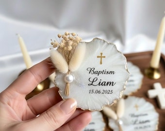 May include: White Baptism favors with gold trim, a cross, and the name "Liam" with the date 15.06.2025. Each favor is decorated with dried flowers and a pearl. The favors are on a wooden tray.