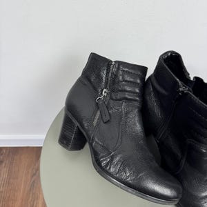 Pu&ograve; includere: Stivaletti in pelle nera con tacco a blocco. Gli stivali hanno una chiusura con zip laterale e pelle strutturata. L'altezza del tacco &egrave; di circa 6,35 cm.