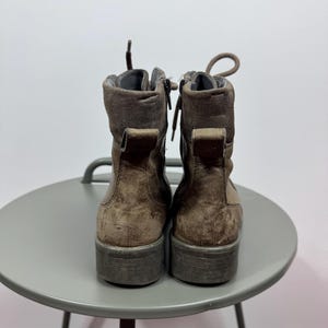 K&ouml;nnte beinhalten: Ein Paar braune Stiefeletten mit Schn&uuml;rung vorne, seitlichen Rei&szlig;verschl&uuml;ssen und einer Zugschlaufe an der Ferse. Die Stiefel haben eine strukturierte Oberfl&auml;che, einen gepolsterten Schaftrand und eine dicke, flache Sohle. Die Schn&uuml;rsenkel sind oben gebunden.