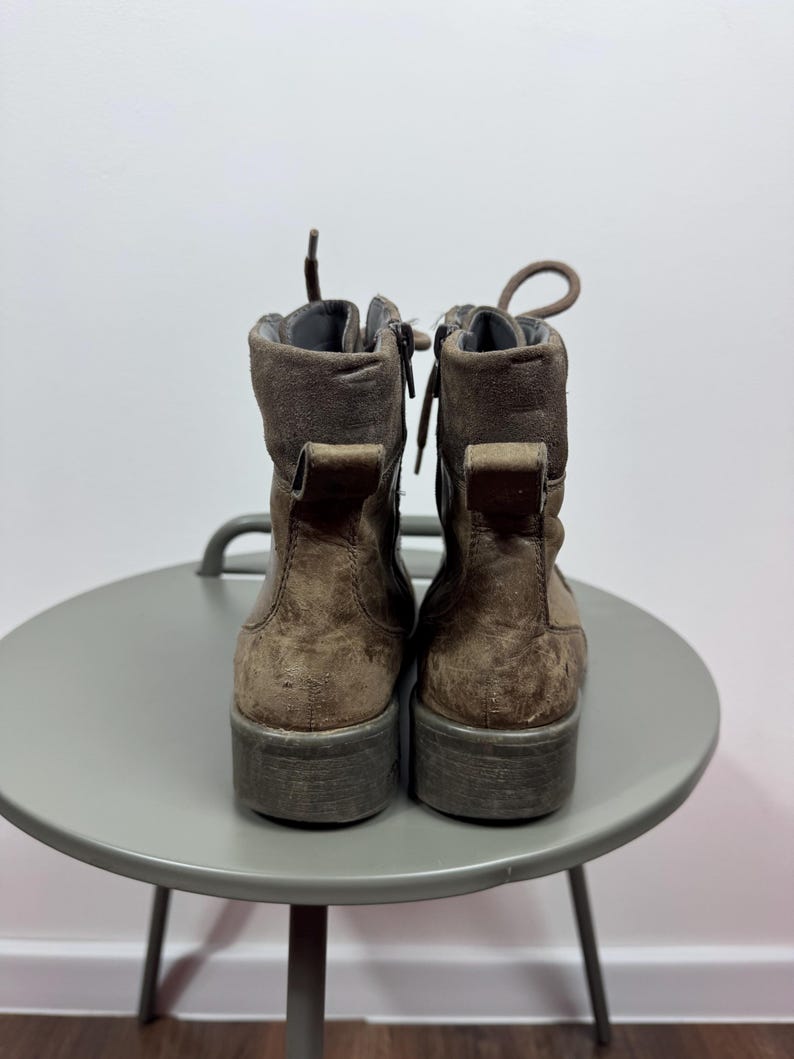K&ouml;nnte beinhalten: Ein Paar braune Stiefeletten mit Schn&uuml;rung vorne, seitlichen Rei&szlig;verschl&uuml;ssen und einer Zugschlaufe an der Ferse. Die Stiefel haben eine strukturierte Oberfl&auml;che, einen gepolsterten Schaftrand und eine dicke, flache Sohle. Die Schn&uuml;rsenkel sind oben gebunden.