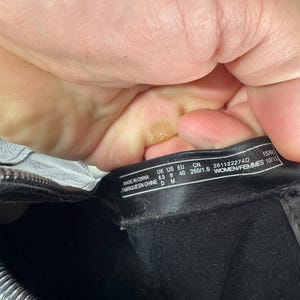 Pu&ograve; includere: Primo piano dell'interno di uno stivale nero con un'etichetta. L'etichetta recita "MADE IN CHINA" ed elenca le taglie: UK 6.5, US 9, EU 40 e CN 250/1.5. &Egrave; visibile anche il testo "WOMEN/FEMMES 10/15".