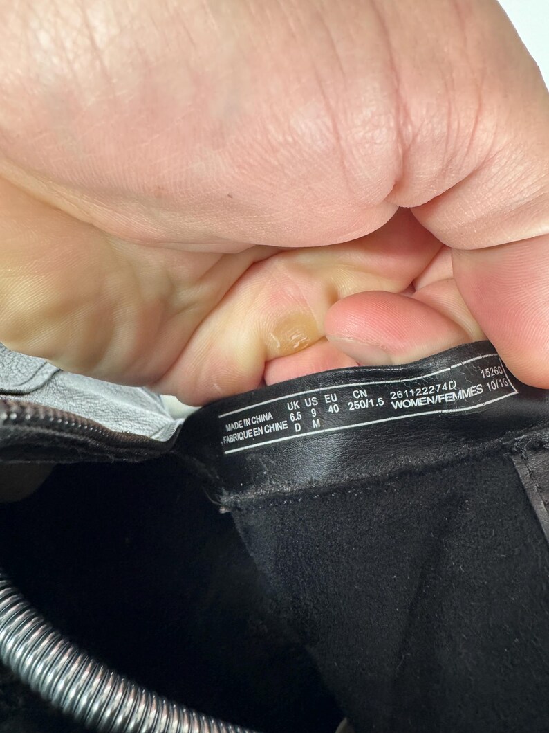 Pu&ograve; includere: Primo piano dell'interno di uno stivale nero con un'etichetta. L'etichetta recita "MADE IN CHINA" ed elenca le taglie: UK 6.5, US 9, EU 40 e CN 250/1.5. &Egrave; visibile anche il testo "WOMEN/FEMMES 10/15".