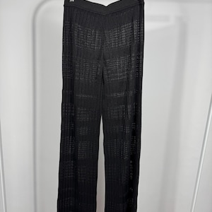 May include: Black, wide-leg pants with a ribbed texture, hanging on a hanger. The pants have a high waist and a slight flare at the hem. The fabric appears to be lightweight and semi-sheer.