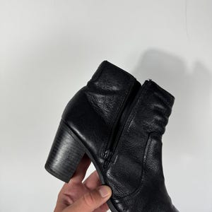 Pu&ograve; includere: Stivaletto alla caviglia in pelle nera con tacco a blocco e zip laterale. Lo stivale ha una superficie strutturata e una punta arrotondata. Il tacco misura circa 7,6 cm.