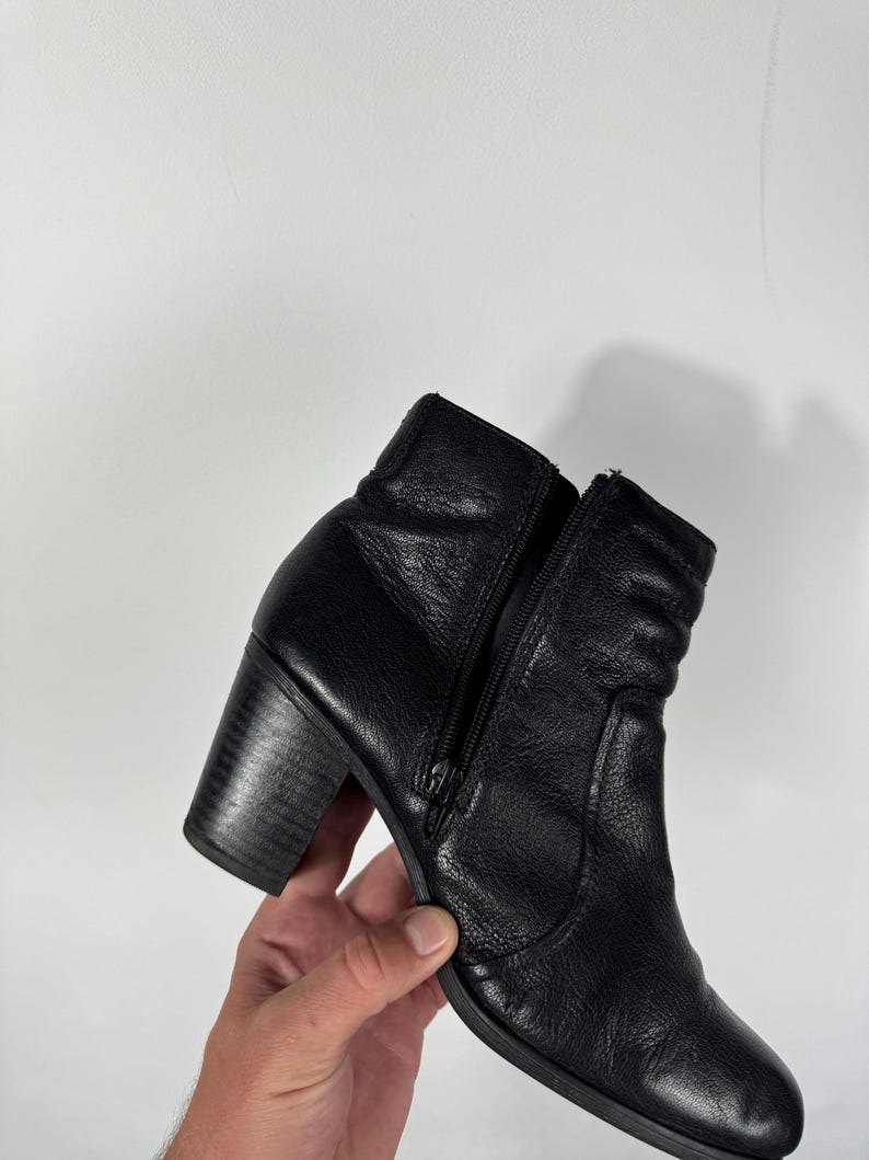 Pu&ograve; includere: Stivaletto alla caviglia in pelle nera con tacco a blocco e zip laterale. Lo stivale ha una superficie strutturata e una punta arrotondata. Il tacco misura circa 7,6 cm.