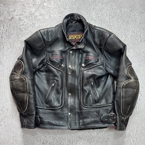Puede incluir: Una chaqueta de moto de cuero negro con cuello alto, cierre frontal de cremallera con botones a presión y dos bolsillos en el pecho con cremallera. La chaqueta incluye coderas reforzadas, correas laterales ajustables con hebillas y el logo Sportex Strada.