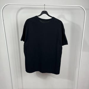 Peut inclure: Un t-shirt noir uni suspendu &agrave; un portant blanc. Le t-shirt est en mati&egrave;re souple et a un col rond. Le t-shirt est pr&eacute;sent&eacute; sur un mur blanc uni.