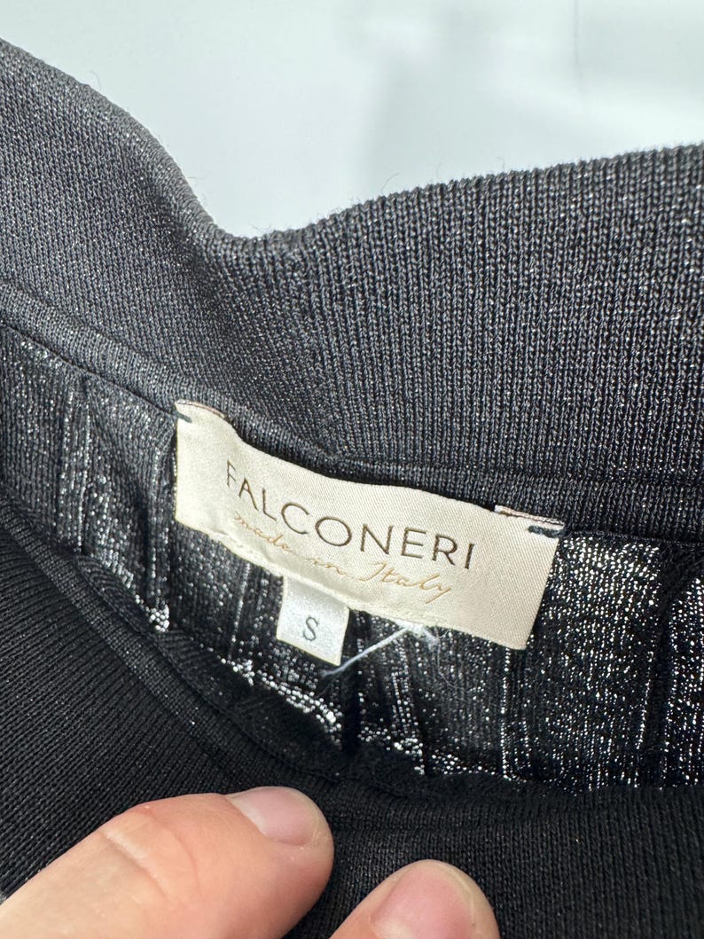 May include: Close-up of a black garment with a ribbed waistband. The label reads "FALCONERI made in Italy" with a size "S" tag. The fabric has a subtle metallic sheen.