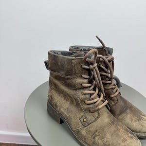 K&ouml;nnte beinhalten: Ein Paar geschn&uuml;rte Stiefel aus braunem Leder in Distressed-Optik mit abgerundeter Zehenpartie, niedrigem Blockabsatz und passenden braunen Schn&uuml;rsenkeln durch Metall&ouml;sen. Die Stiefel haben eine strukturierte, abgenutzte Oberfl&auml;che und einen seitlichen Rei&szlig;verschluss.