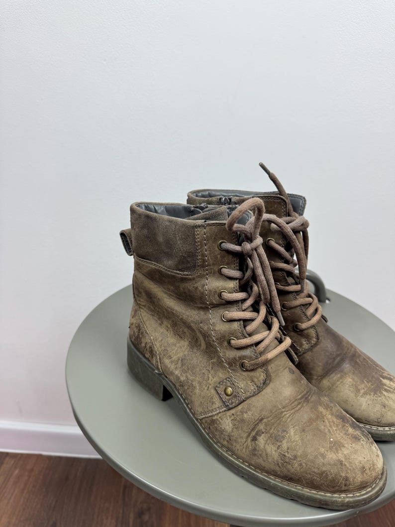 K&ouml;nnte beinhalten: Ein Paar geschn&uuml;rte Stiefel aus braunem Leder in Distressed-Optik mit abgerundeter Zehenpartie, niedrigem Blockabsatz und passenden braunen Schn&uuml;rsenkeln durch Metall&ouml;sen. Die Stiefel haben eine strukturierte, abgenutzte Oberfl&auml;che und einen seitlichen Rei&szlig;verschluss.