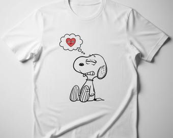 Könnte beinhalten: Weißes T-Shirt mit einer Schwarz-Weiß-Illustration von Snoopy. Snoopy wird mit einer Sprechblase mit einem roten Herzen dargestellt. Die Comicfigur sitzt mit besorgtem Gesichtsausdruck da. Das T-Shirt ist aus weichem Material.