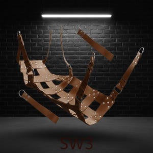A brown leather sling with a woven design, metal rings and straps. The product is suspended in the air against a dark brick wall background. The letters "SW3" are visible at the bottom.